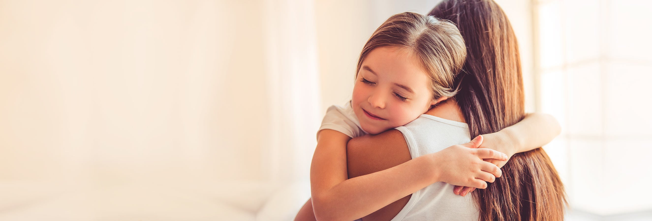 Pige med lukkede øjne giver en kærlig krammer til en voksen person med langt hår.