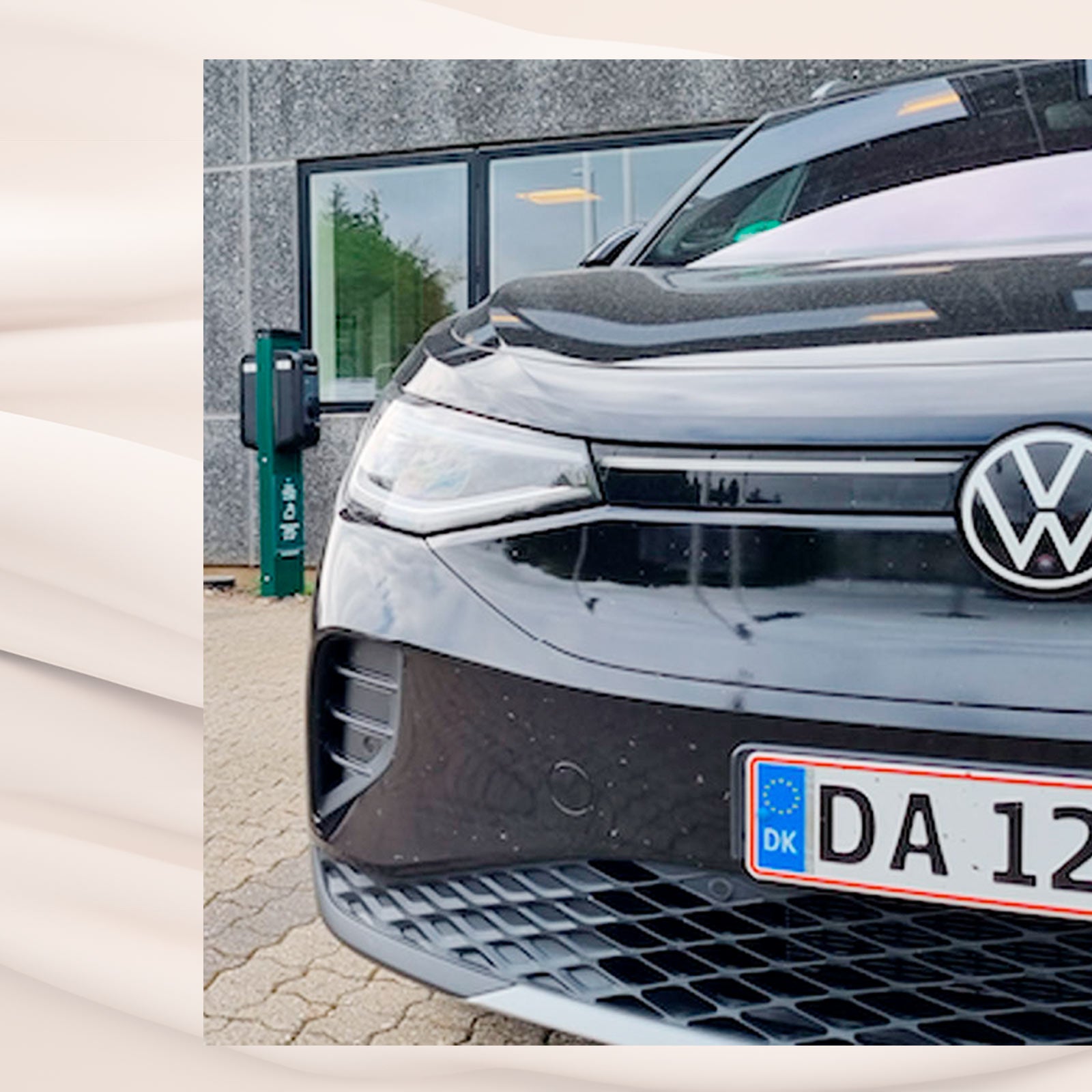Sort Volkswagen elbil parkeret foran bygning med ladestander i baggrunden.