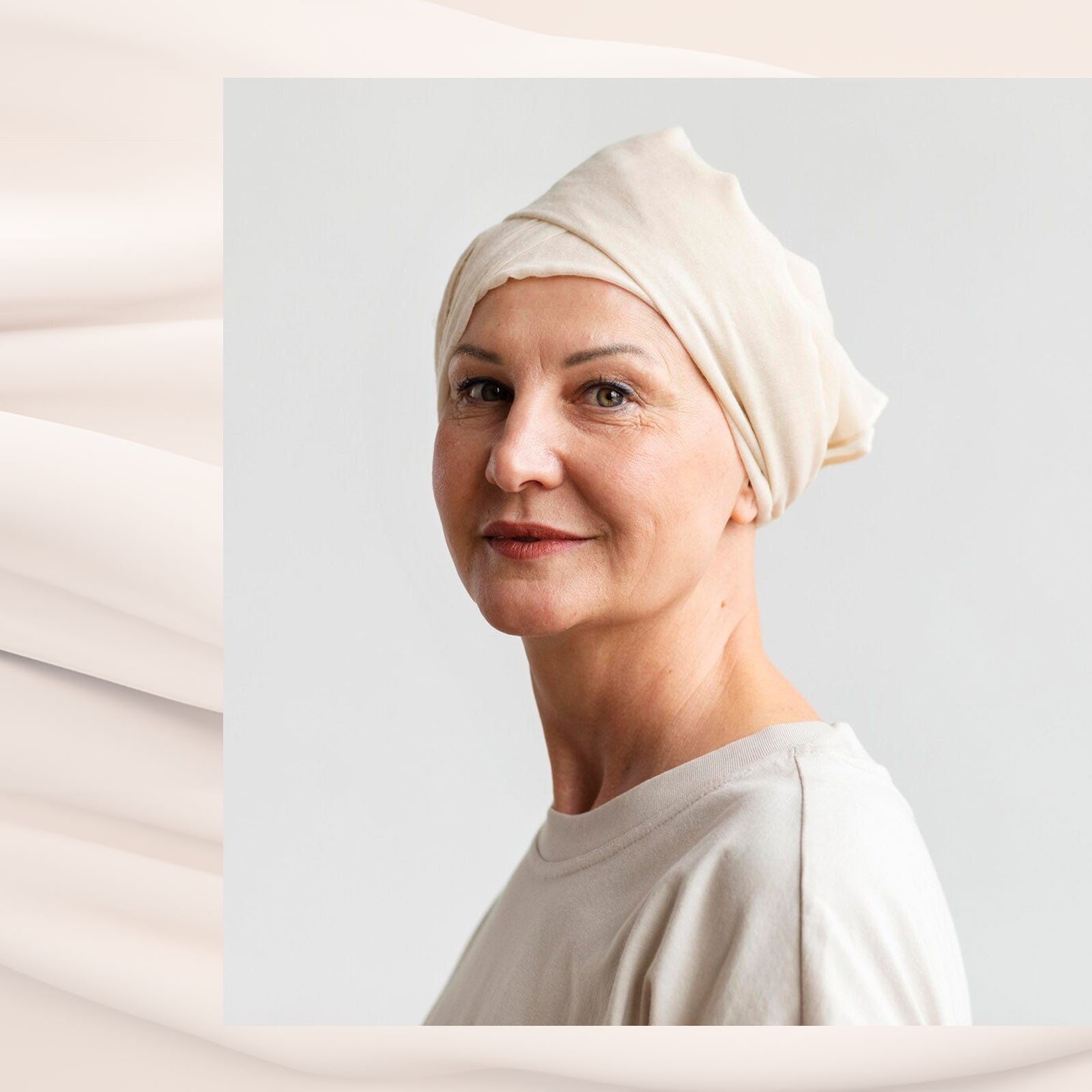 Smilende kvinde med tørklæde på hovedet iført lyse klæder foran lys baggrund.