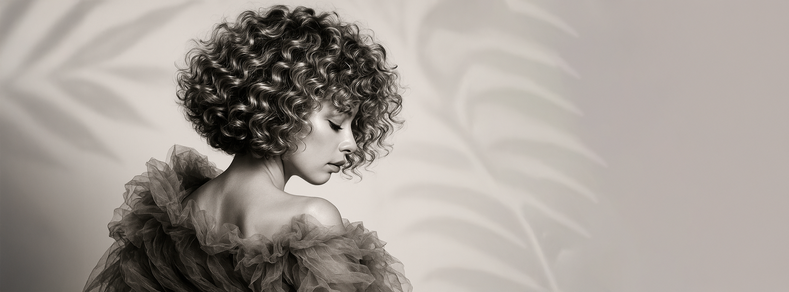 Kvinde med kort, naturligt krøllet hår set fra siden i sort-hvid æstetik.