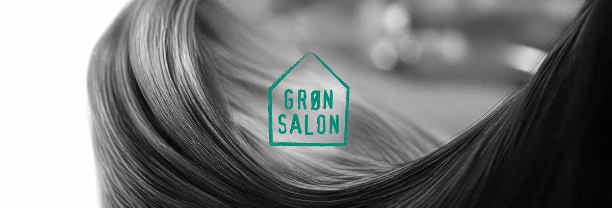 I forgrunden ses IdHAIRs logo for Godkendt til Grøn Salon. I baggrunden ses sort hår på hvid baggrund