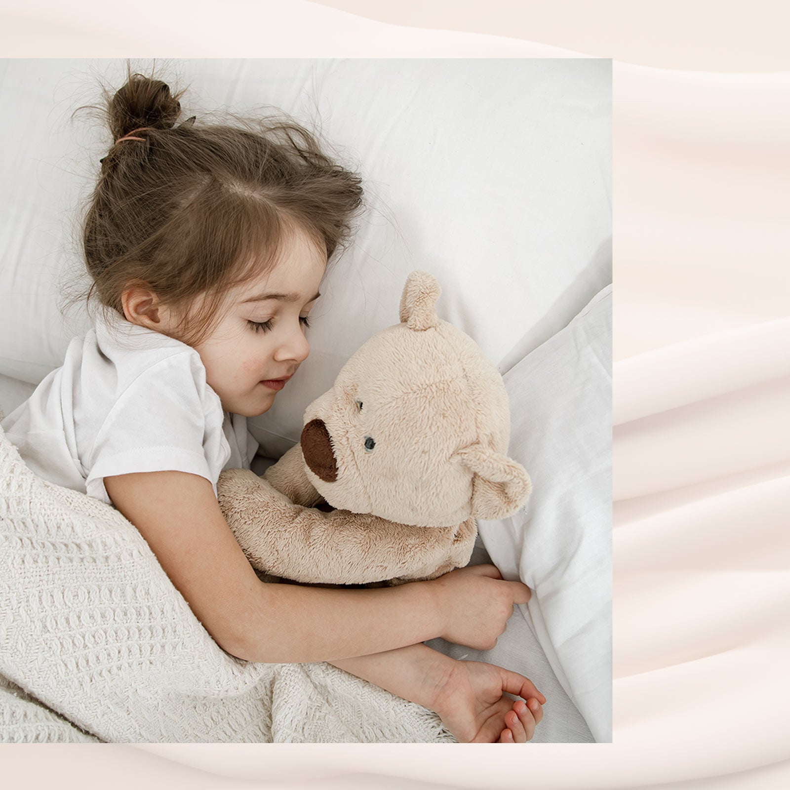 Lille pige sover trygt i hvid seng med hvidt sengetøj og bamse i armene.