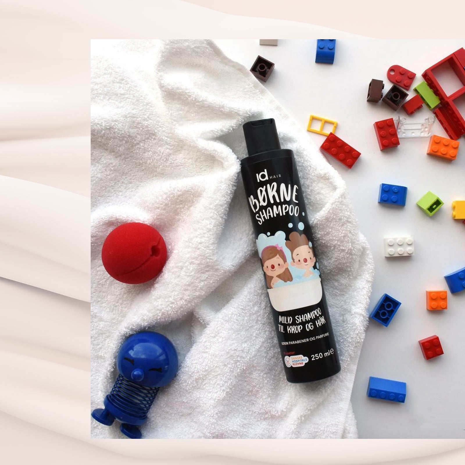 IdHAIR Børne Shampoo ligger på hvidt håndklæde omgivet af farverige byggeklodser og legetøj.