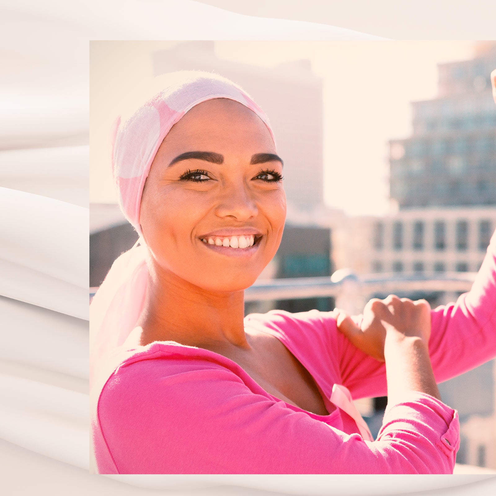 Smilende kvinde med tørklæde og lyserød trøje strækker armene ud på en solrig tagterrasse.