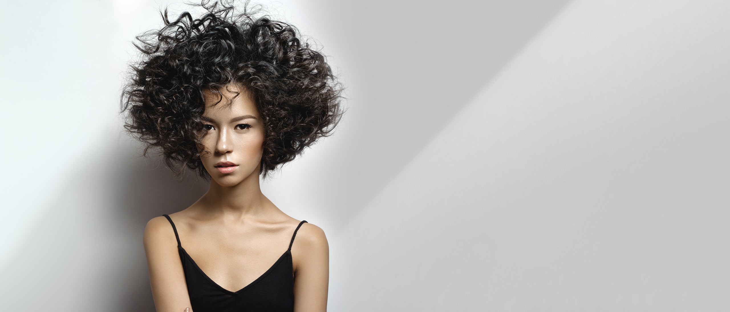 Kvinde med voluminøst mørkt krøllet hår mod lys baggrund.