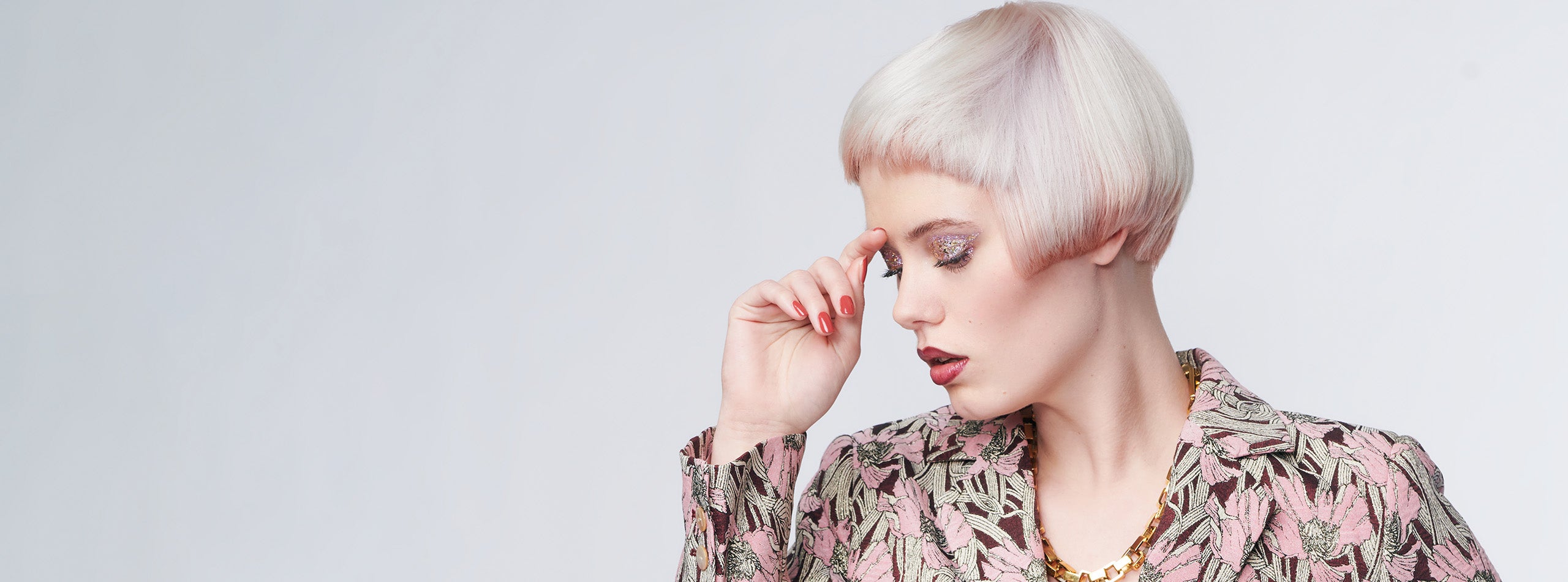 Kvinde med kort, platinblond page og glittermakeup mod lys baggrund.