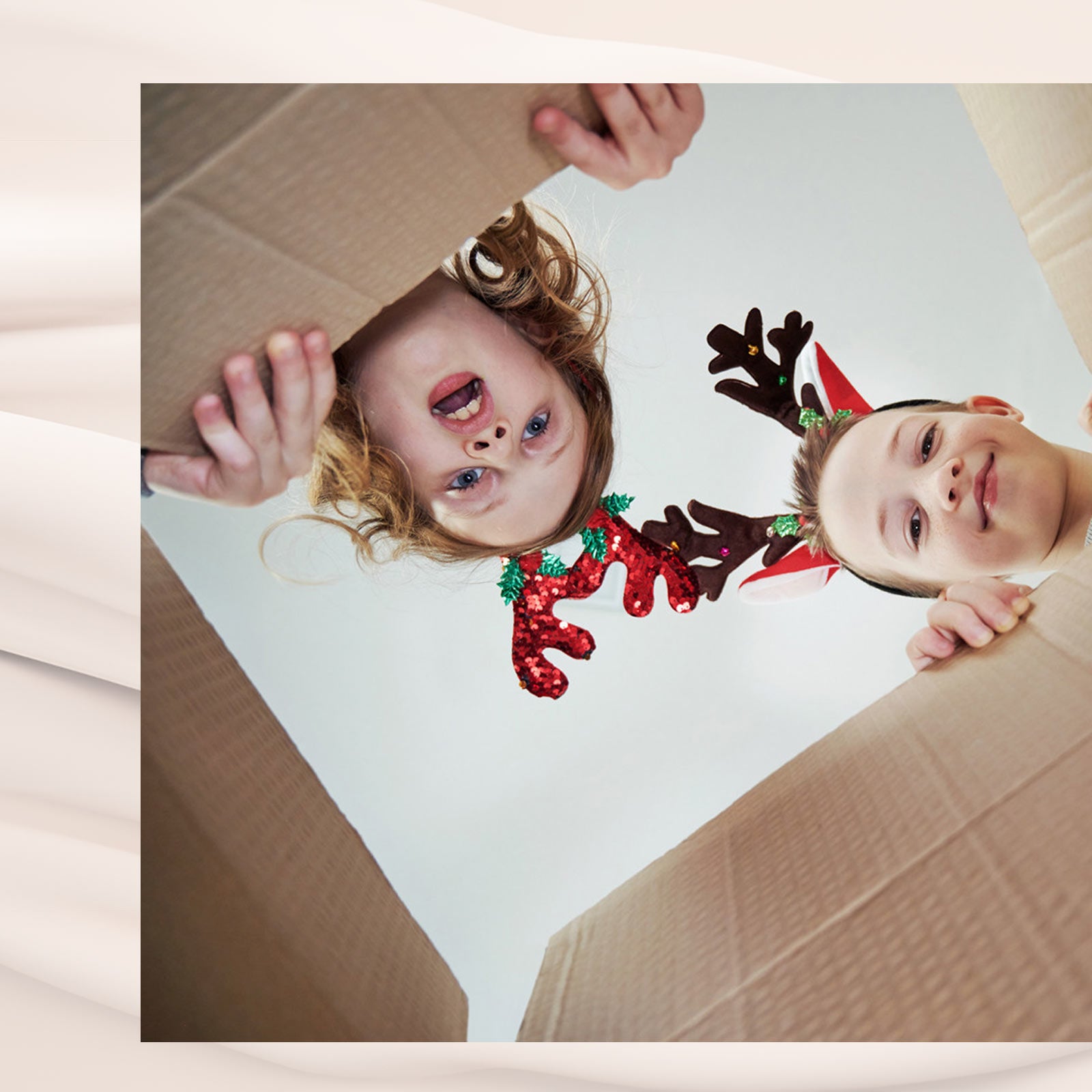 To børn med rensdyrhorn kigger spændt ned i en papkasse med juleudtryk i ansigterne.
